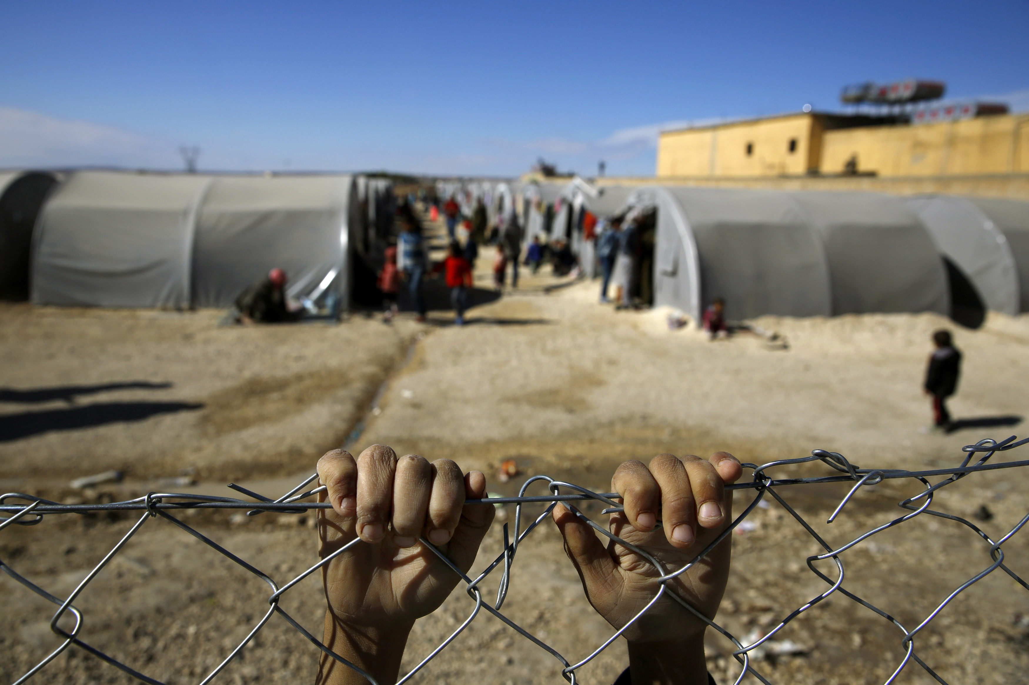 Kurdish refugee boy from the Syrian town of Kobani holds onto a fence that surrounds a refugee camp in the border town of Suruc, Sanliurfa province